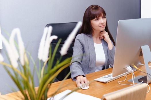 A brunette woman at a computer in the workplace. Business concept.