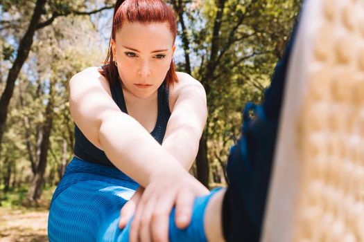 young woman practicing stretching exercises to gain flexibility outdoors. sporty woman preparing for a marathon. health and wellness lifestyle. Natural sunlight, background of natural vegetation, forest, sportswear.