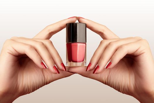 Manicured nails with red nail polish. Manicure with bright nailpolish. Fashion manicure. Shiny lacquer in bottle. Hands hold bottle of gel polish