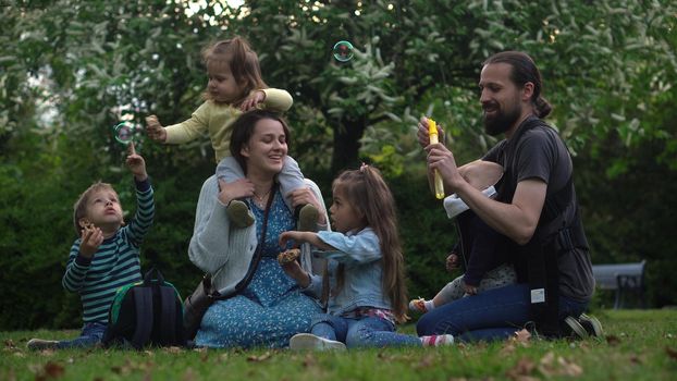 Happy family mother Father Three four Baby little siblings kids have fun blowing bubbles enjoying summer holidays in garden park. Smiling parents children spending leisure time together evening sunset.