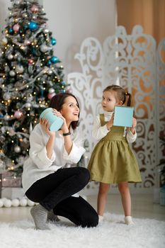 Cute little girl with her mother give each other new year gifts in christmas interior. Vertical, copy space.