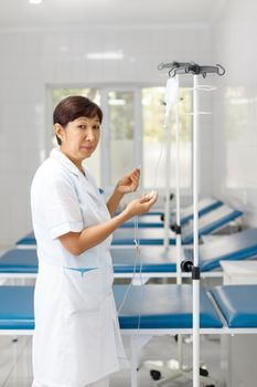 Vertical portrait of a senior female nurse in middle asia Kazakhstan clinic intravenous drip hospital room.