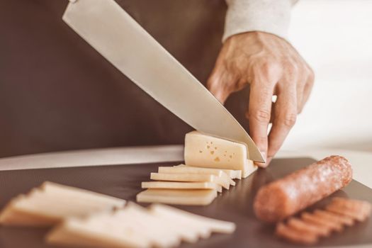 close up. man slicing cheese and salami for sandwiches