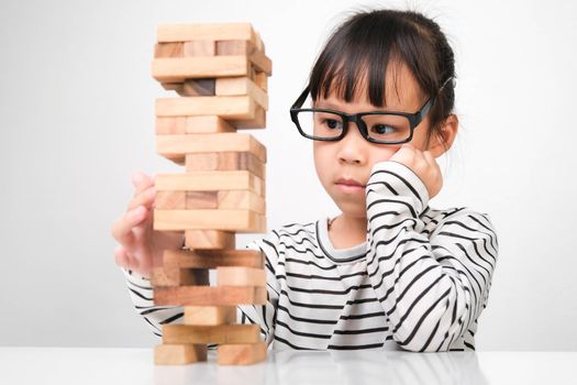 Asian children playing wooden blocks on table at home. Cute little girl having fun playing with building blocks. Wooden block tower building game. Toys for the development of children