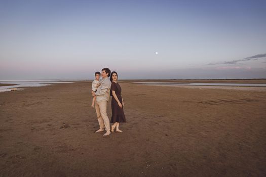 Beautiful young family on the evening beach. Family look of natural linen clothing. Copy space.