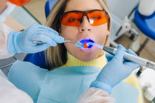 A young beautiful girl in dental glasses treats her teeth at the dentist with ultraviolet light. filling of teeth.