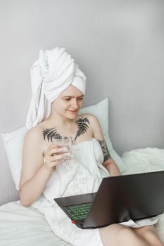 Tver, Russia-august 2, 2021. A tattooed woman after a shower is lying on the couch with a laptop. The concept of multitasking in the modern world. Self-care and work from home. The need for gadgets in the life of a millennium