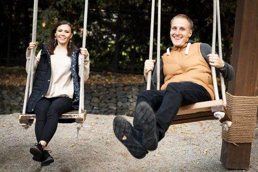 Young interracial happy couple swinging on a swing in autumn in light clothes outdoors in the park. High quality photo