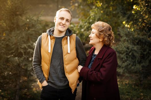 Loving mature mom with her adult son among the trees autumn outdoors.