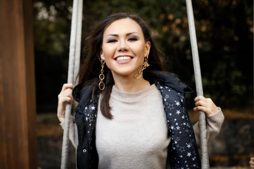 Close-up portrait of a young cheerful tatar woman swinging on a swing in the forest in autumn. High quality photo