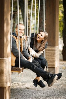 Side view of happy laughing couple sitting on swing in park outdoors. High quality photo