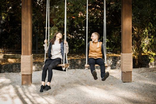 The first ridiculous date of a young couple in an autumn park on a swing.
