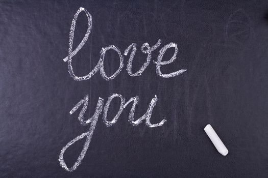 Inscription I Love You and chalk piece on black stone background. Love message.