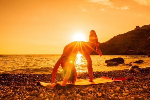 Young woman with black hair, fitness instructor in pink sports leggings and tops, doing pilates on yoga mat with magic pilates ring by the sea on the beach. Female fitness daily yoga concept