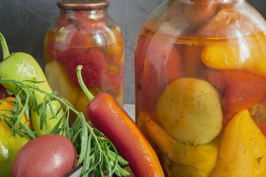 In glass jars, canned bell peppers, next to a box of peppers and other vegetables. Front view, close-up