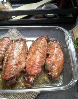 On a wooden table on a napkin is a tray with baked Turkey wings. Next to it are spices and herbs