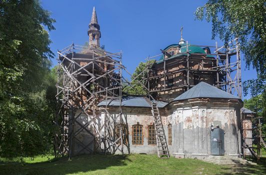 A small Orthodox old Church in the countryside is surrounded by scaffolding and restoration works are carried out.