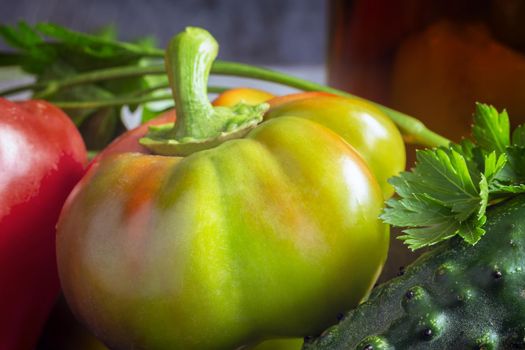 Large ripe bell pepper fruit next to tomato, cucumber and parsley.