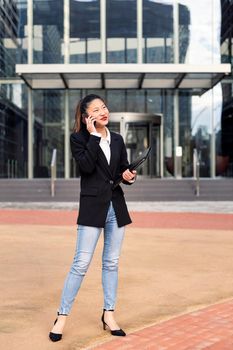 asiatic business woman talking by phone in front of an office building, concept of work and communication, copy space for text