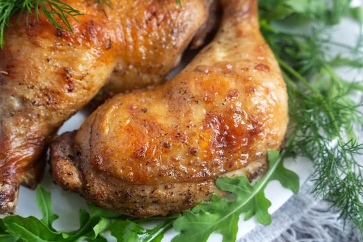 On the table on a linen napkin is a plate with baked chicken legs and herbs. Presented in close-up.