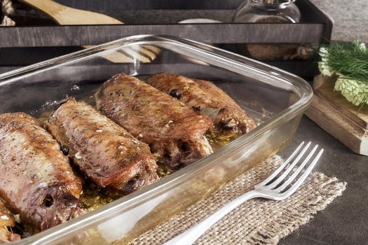 On a wooden table on a napkin is a tray with baked Turkey wings. Next to it are spices and herbs