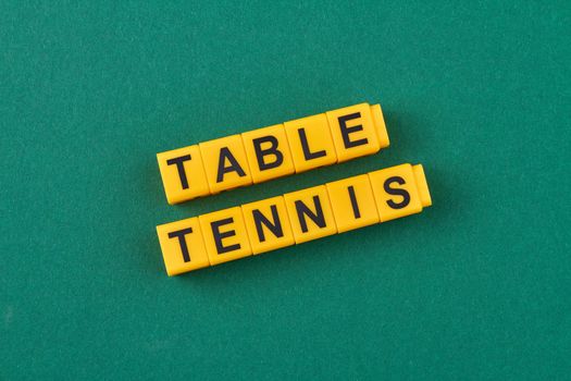The inscription table tennis written on yellow cubes against green background. Flat lay.