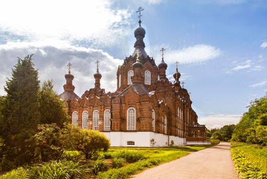 A beautiful Orthodox temple located on a hill surrounded by flowers and plants: arborvitae, blue spruce, shrubs.