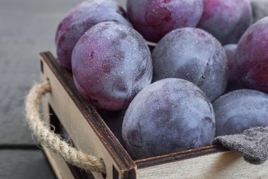 On the table in a drawer are large ripe plums. Presented in close-up on a dark background. The view from the top.