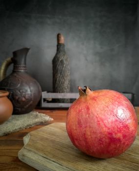 On the kitchen table on the cutting Board is a large ripe pomegranate fruit. Next to it is a kitchen knife. A dark background and copy space.