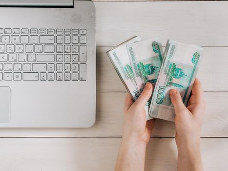Hands holding russian rubles near laptop on white wooden background. Top view or flat lay. Finance and earning concept