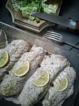 Marinated Turkey wings in a tray on a wooden table, prepared for roasting in the oven. There are spices and herbs nearby.