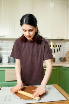 Young brunette woman knead the dough for shortcrust pastry on a baking mat, vertical.