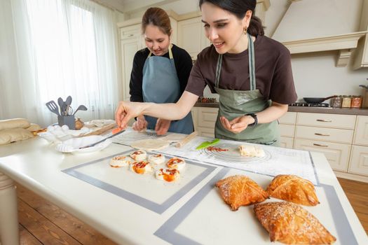 Two young women preparing homemade cakes on silicone baking mats in a large bright kitchen.