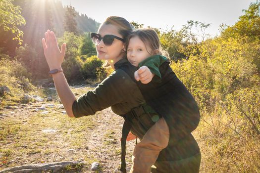 Babywearing mother with her daughter in ergonomic back sling in sunny day of summer outdoor.