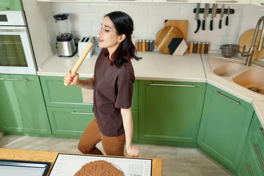 Young happy joyful brunette cooking homemade cookies while dancing.