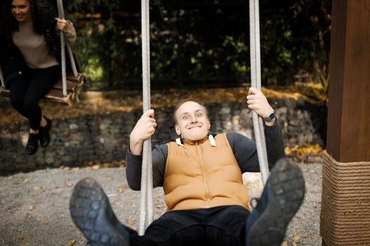 Young man having fun with his beloved swinging on a swing with high legs outdoor. High quality photo