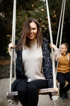 Happy young mixed race couple on a date swinging on a swing, in the foreground is a woman with straight hair and a snow-white smile, in the background a smiling young man