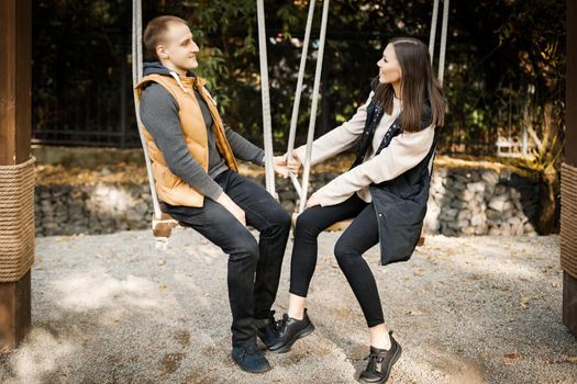 Young couple on a date cute talking while sitting on a swing in the forest among the trees. High quality photo