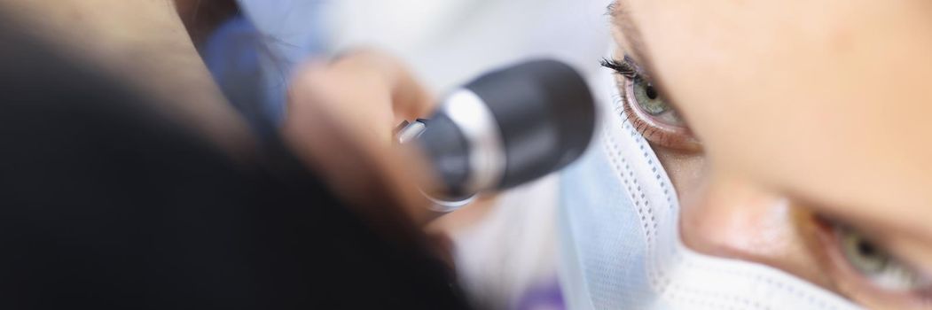 Top view of female ent doctor in medical mask examining ear with otoscope carefully. Patient at practitioner appointment. Otolaryngology, medicine and healthcare concept