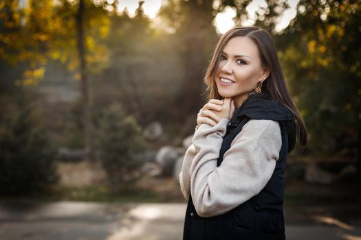 Portrait of a cute young woman among the autumn foliage in the park in a sweater and a warm vest. High quality photo