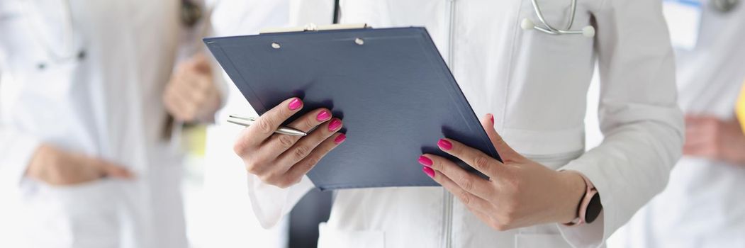 Close-up of therapist hands holding clipboard. Team of doctors in white gowns. Physician with colleagues in clinic. Healthcare, teamwork and medicine concept