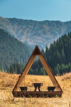 Modern gazebo on a tourist trail with a scenic view of the summer mountains with a spruce forest, vertical copy space.
