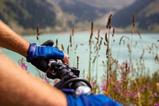 Close-up of hands in sports gloves on the handlebars of a mountain bike against the backdrop of a mountain lake.