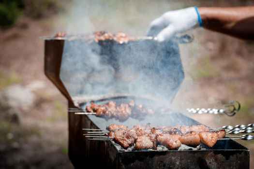 View of the hands of a barbeque cook who fries meat on skewers on the grill outdoor.