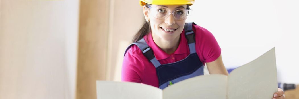 Portrait of smiling female holding blueprint and looking at camera with happiness. Cheerful architect working at new construction project. Architecture and building concept