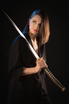 Portrait of a young kung fu brunette girl in a kimono with a Japanese sword on a black background.