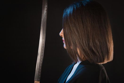 Portrait of a young woman in front of a sharp blade on a black background.