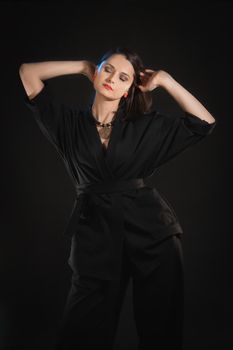 Studio shot in low key with woman with raised hands in black clothes.