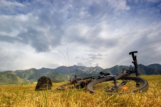 The mountain bike lies on the meadows next to the backpack in the foothills. Bike travel light, copy space.