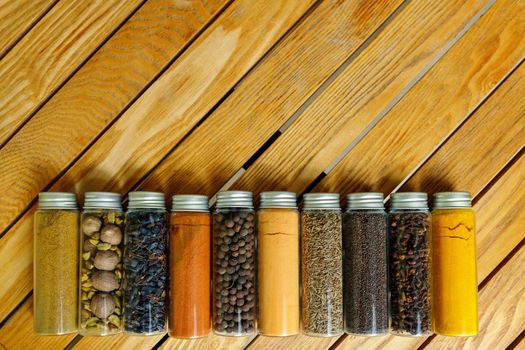 Different multi-colored indian spices in transparent jars lie on a wooden background with copy space.